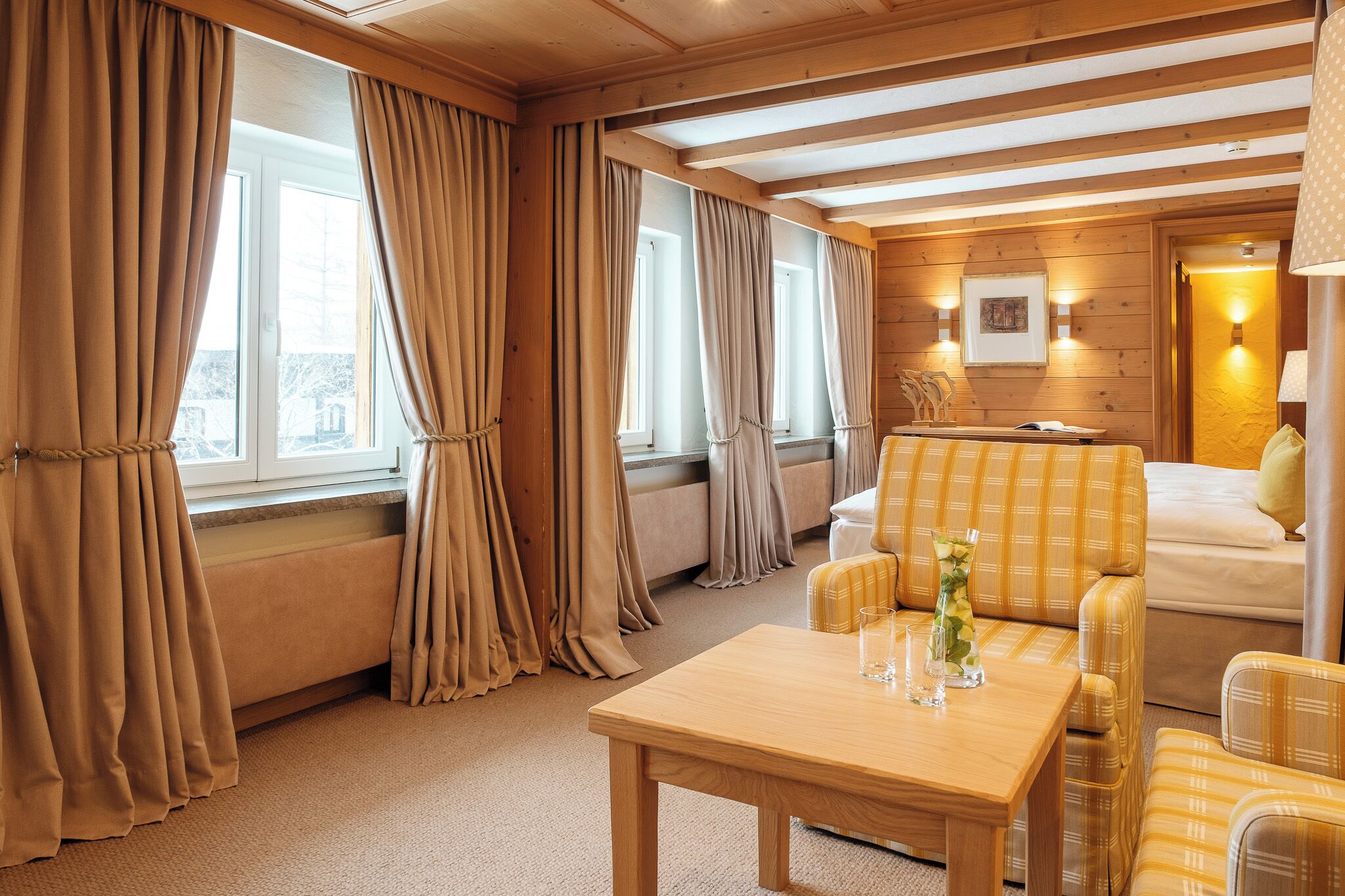 A cozy room with a wooden ceiling, a sofa, a table, and curtains.