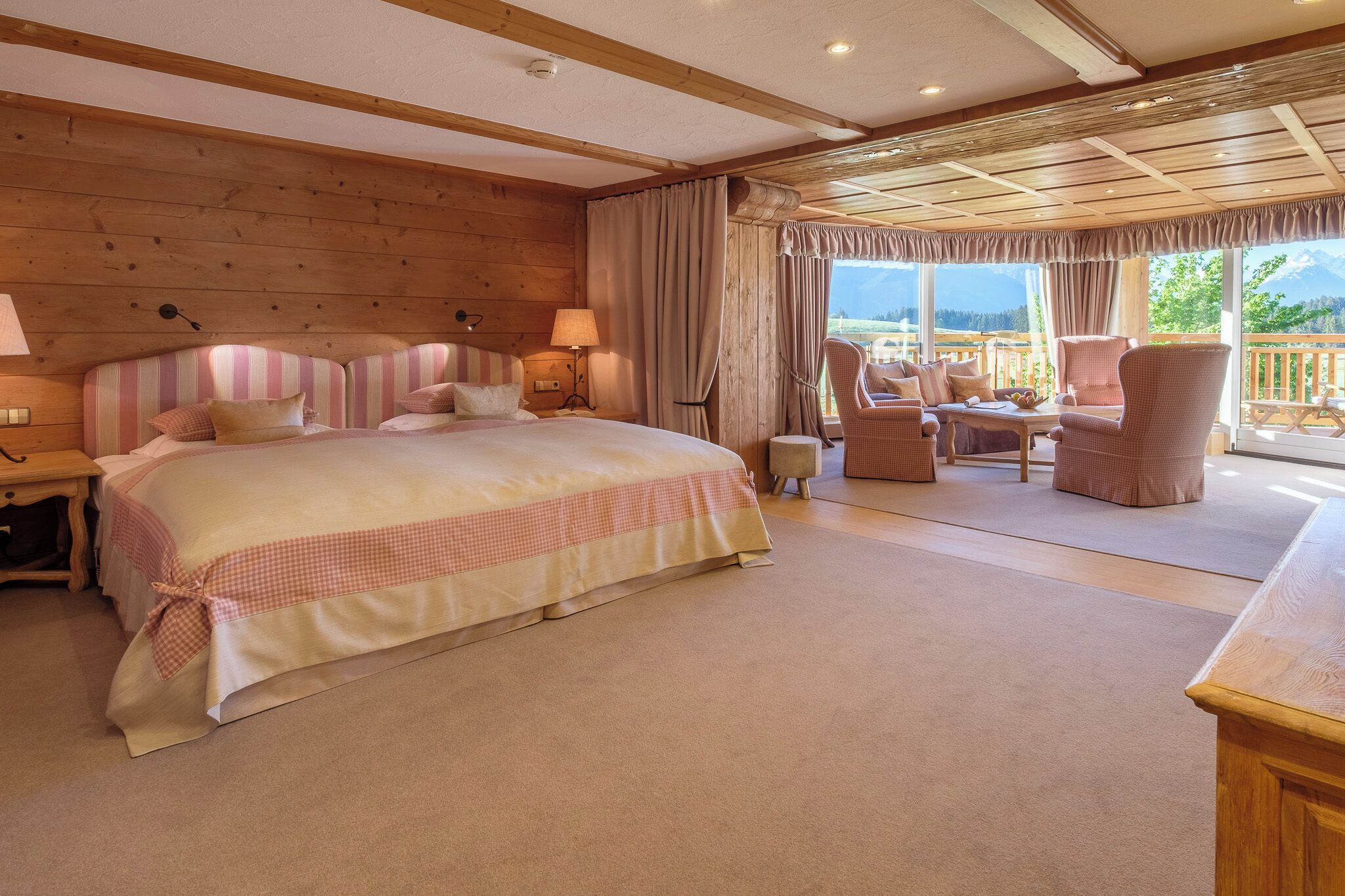 A bedroom with a large bed, a sitting area with chairs, and a view of the mountains.