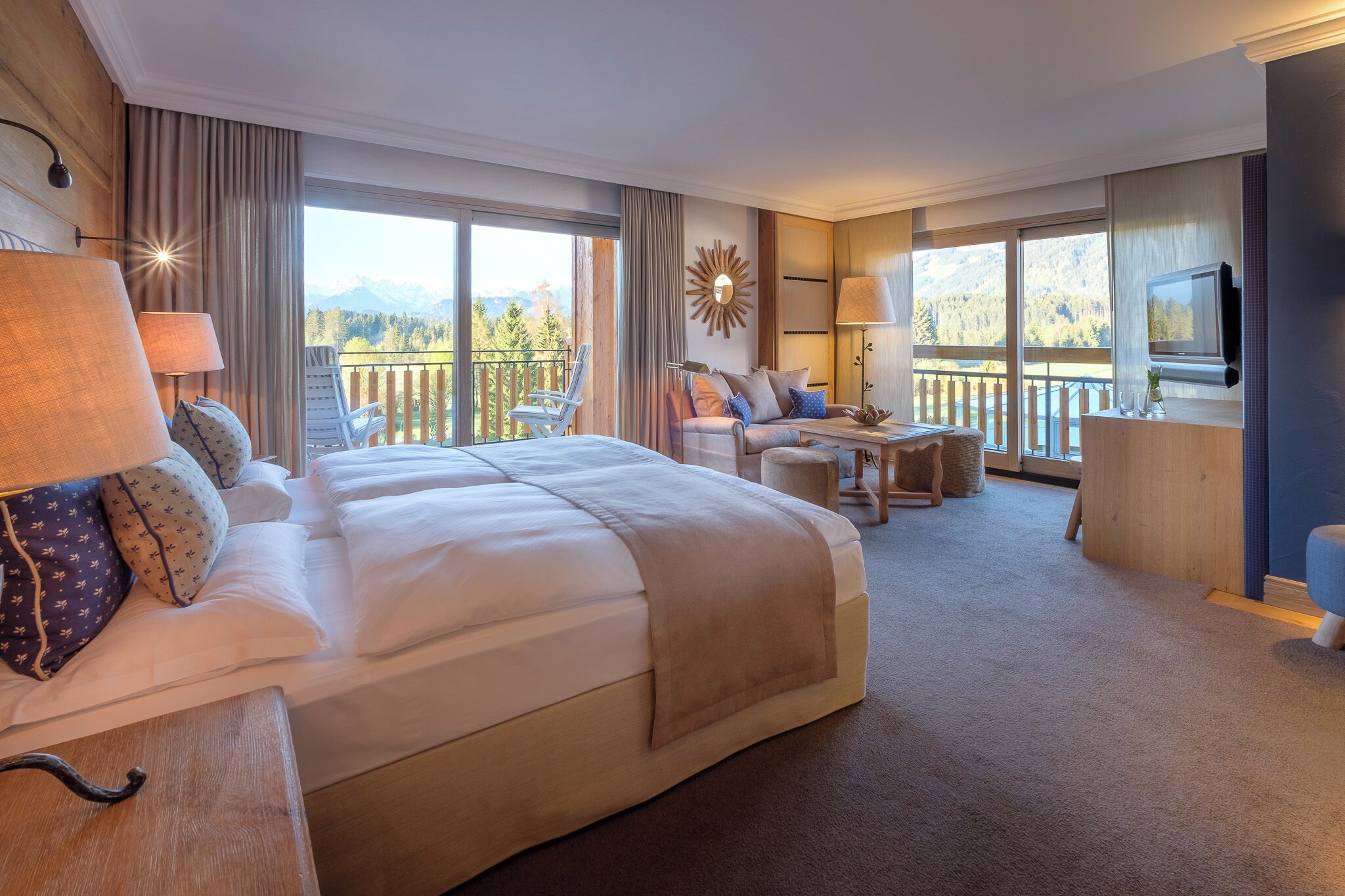 Ein Hotelzimmer mit einem großen Bett, einer Sitzecke mit einem Tisch und einem Balkon mit Bergblick.