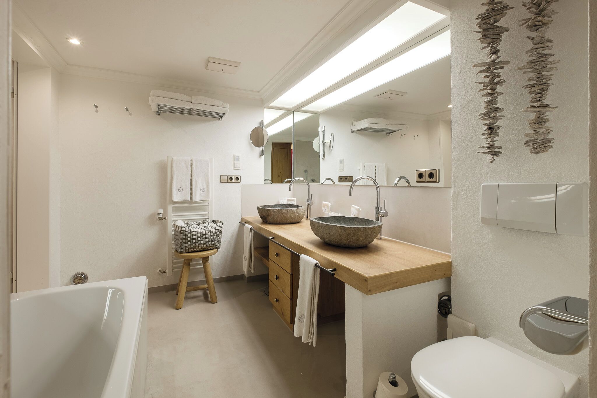 A modern bathroom with a bathtub, a wooden vanity with two large bowls, a toilet, and a mirror.