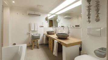 A modern bathroom with a bathtub, a wooden vanity with two large bowls, a toilet, and a mirror.
