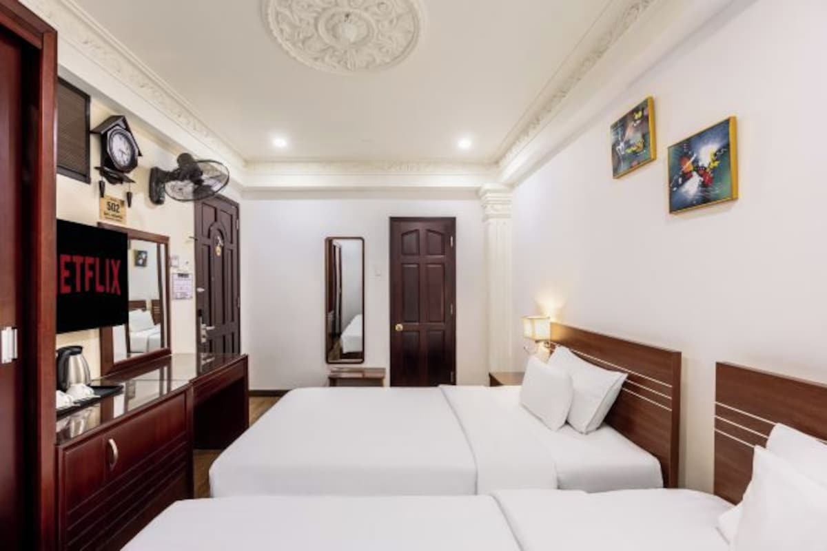 A hotel room with two beds, a TV, a mirror, and a door.