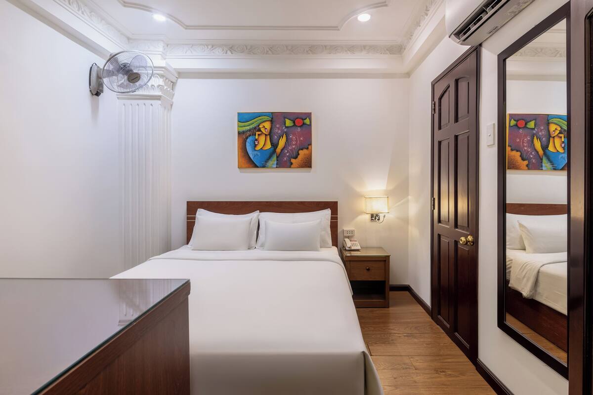 Ein Hotelzimmer mit einem großen Bett, einem Nachttisch mit Lampe, einer Wandklimaanlage und zwei Bildern an der Wand.