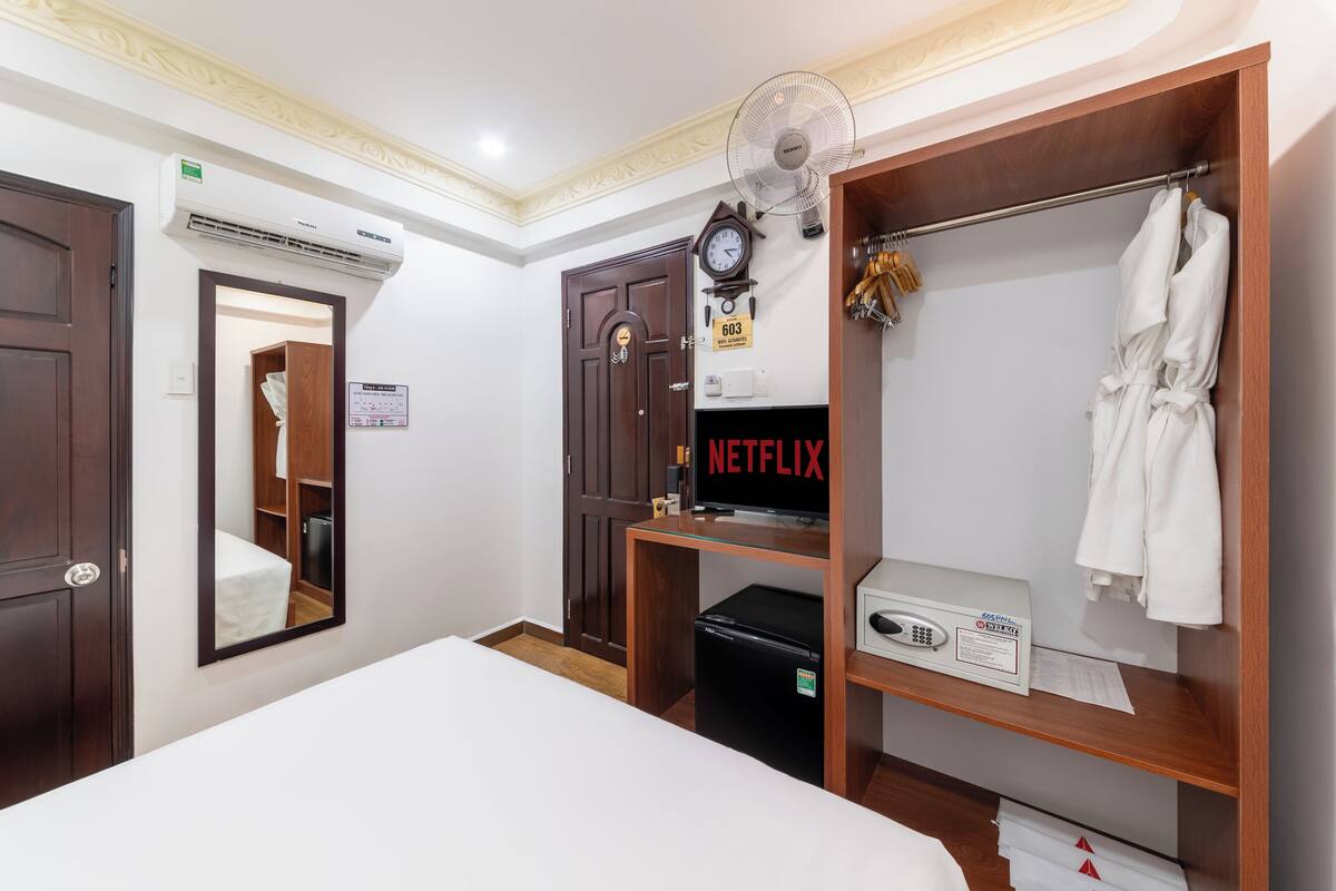 Ein Hotelzimmer mit Bett, Kleiderschrank, Spiegel, Uhr, Ventilator und einem Schild mit der Zimmernummer 603.