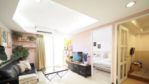 A modern living room with a glass coffee table, a black leather sofa, a TV, and a bed with a white headboard. - SOGO Dept. Zhongxiao Fuxing MRT (Taipei)