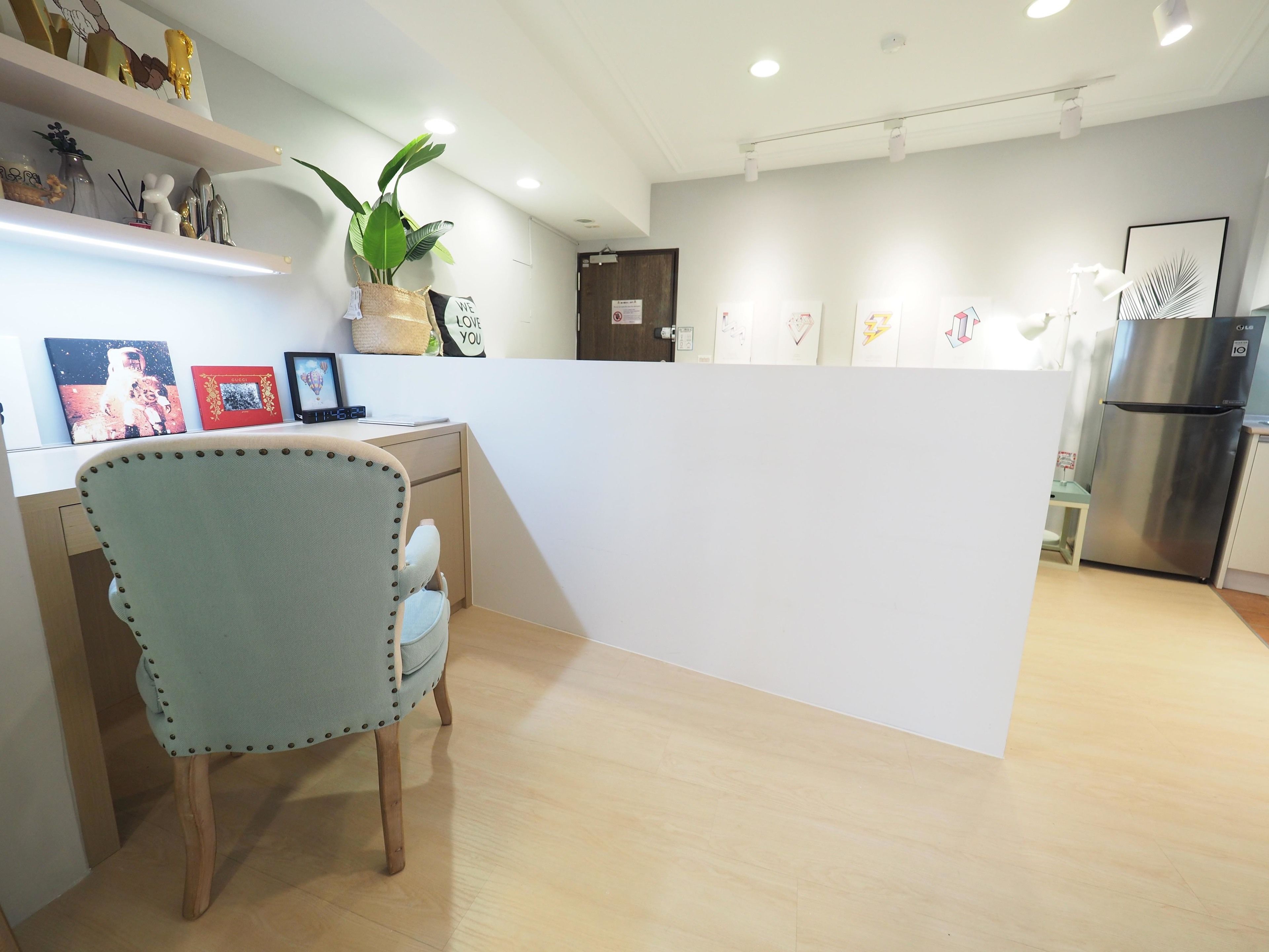 A modern kitchen with wooden flooring, a refrigerator, and a dining area with a chair and a table.