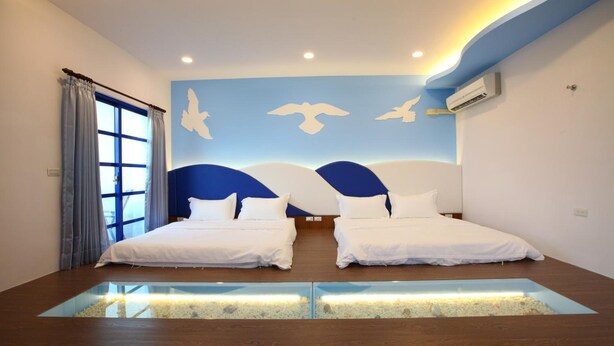 A modern hotel room with two beds, a large window with curtains, a wall mural with birds, and a built-in aquarium. - Easy Stay B&B (Magong)