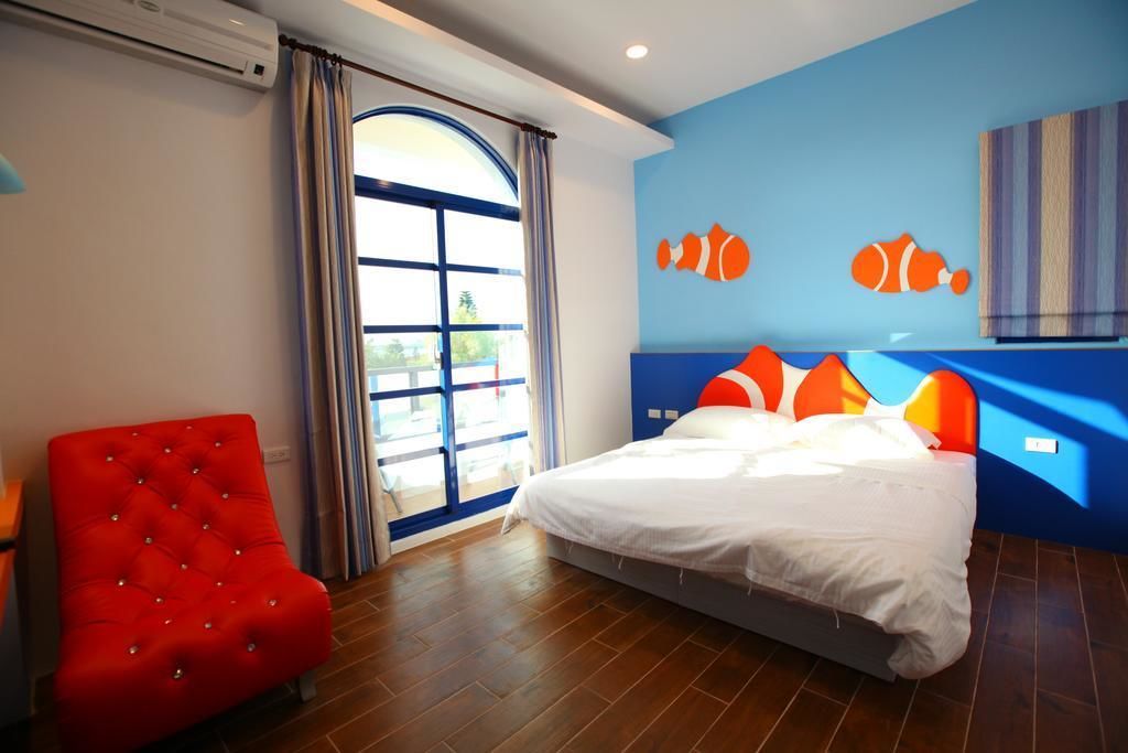 A bedroom with a bed, a red chair, and a window with curtains.