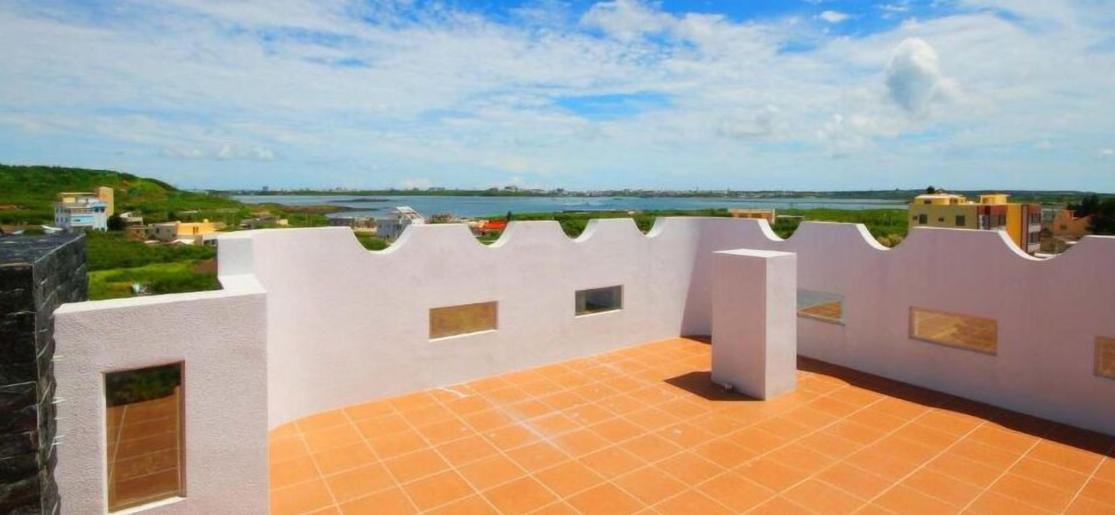 A rooftop terrace with a view of a body of water and distant buildings.