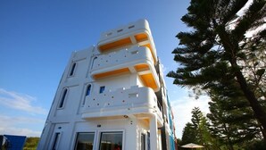 A multi-story building with balconies, a dining area with outdoor seating, and a clear sky. - Easy Stay B&B (Magong)