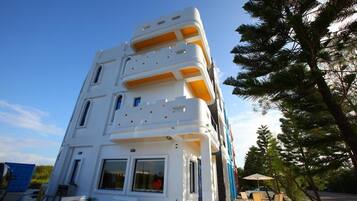 A multi-story building with balconies, a dining area with outdoor seating, and a clear sky.