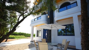 A modern two-story building with a patio area featuring a round table and chairs, an umbrella, and a view of the surrounding landscape. - Easy Stay B&B (Magong)