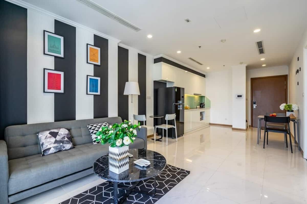 A modern living room with a sofa, a coffee table with a vase of flowers, and a dining area with chairs and a table.