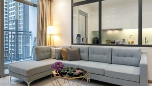 A modern living room with a grey sofa, a small coffee table, and a view of a cityscape through large windows.