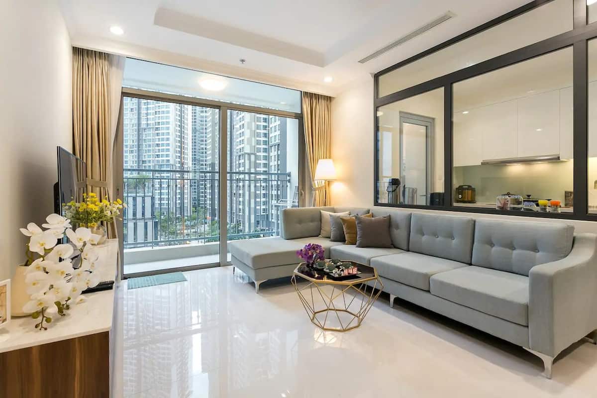A modern living room with a grey sofa, a coffee table, and a large window with a city view.