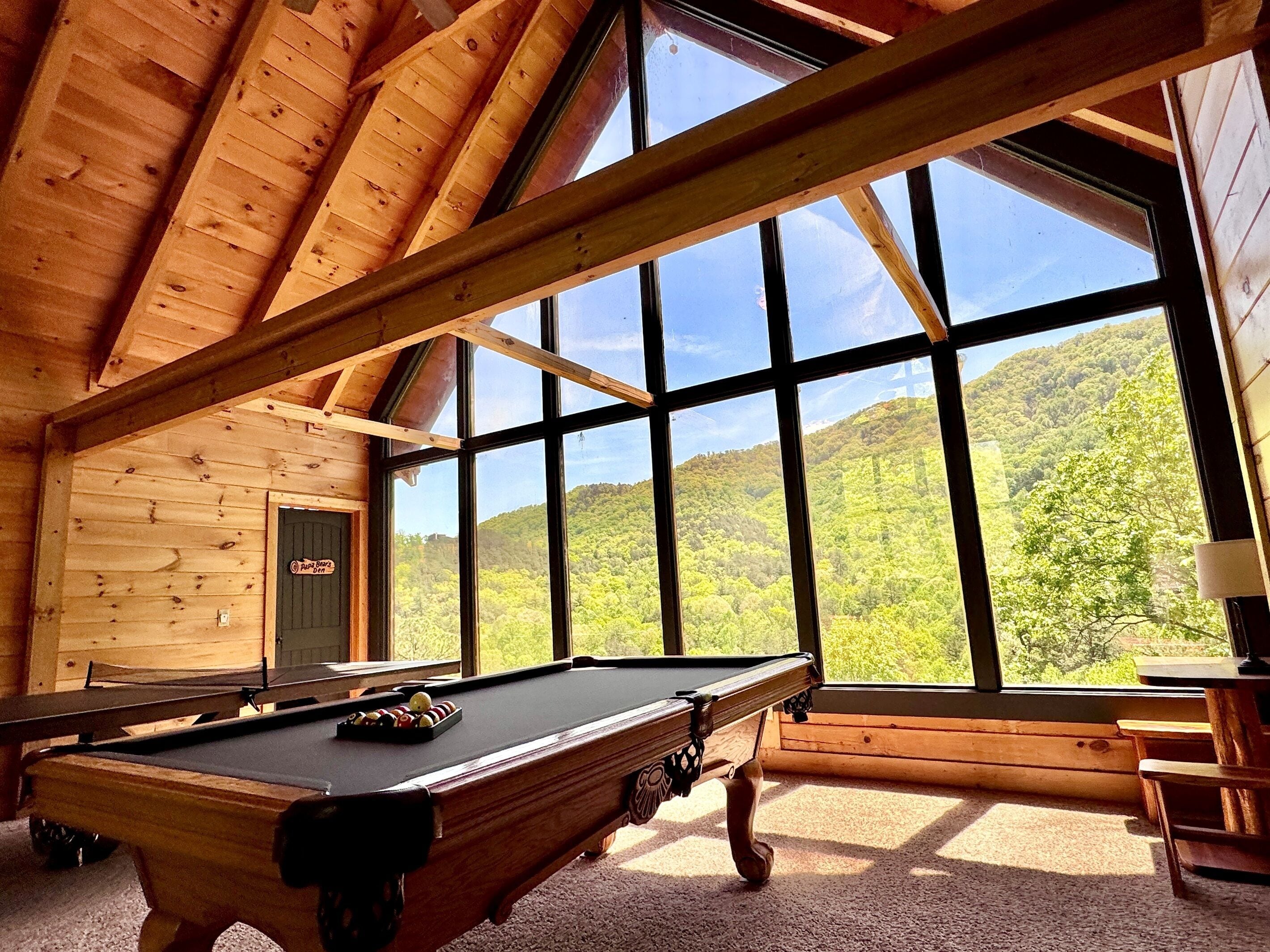 A pool table in a room with large windows and wooden walls.