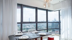 A dining area with a table set for four, large windows offering a city view, and a red bench. - OYO Home 89396 Indescribable 3br Arte Plus (Kuala Lumpur)