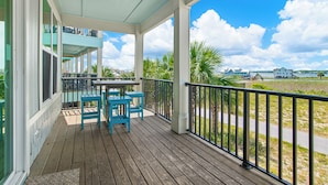 A covered outdoor area with a wooden deck, outdoor furniture, and a view of a body of water and distant buildings. - Lagoon Views | Steps to Gulf Access | Community Pool and Pier (gulf shores)
