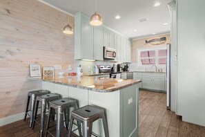 A modern kitchen with a central island, bar stools, stainless steel appliances, and a wooden accent wall. - Lagoon Views | Steps to Gulf Access | Community Pool and Pier (gulf shores)