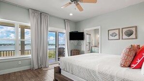 A bedroom with a large bed, a ceiling fan, a TV, and a view of the outdoors. - Lagoon Views | Steps to Gulf Access | Community Pool and Pier (gulf shores)