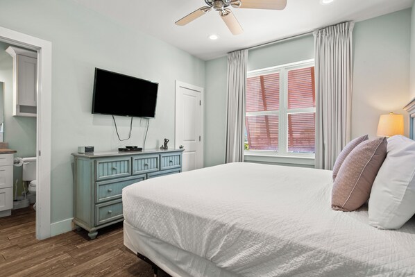 A bedroom with a bed, a dresser, a television, and a window with curtains.