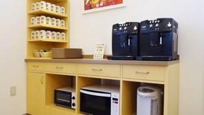 Una kitchenette con un microondas, una olla arrocera y dos cafeteras sobre un mueble amarillo.