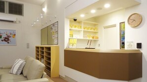 Un área de recepción con mostrador, estanterías con objetos amarillos, un reloj y un cuadro en la pared.