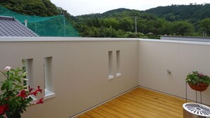 A rooftop terrace with a wooden floor, beige walls, and two small windows. - Family Lodge Hatagoya Niihama (Niihama)
