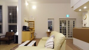 A hotel lobby with a reception desk, a sofa, a coffee station, and a door with an exit sign. - Family Lodge Hatagoya Niihama (Niihama)