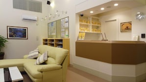 Zona reception con un divano beige, una scrivania, scaffali con oggetti gialli, un orologio e un quadro appeso al muro.