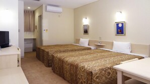 Una camera d'albergo con due letti singoli, una scrivania, un televisore e un angolo cottura.