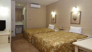 Quarto de hotel com duas camas, televisão, escrivaninha e pequeno espaço de cozinha.