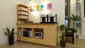 Uma cozinha compacta com micro-ondas, torradeira e cafeteira, uma prateleira com potes e uma planta em vaso.