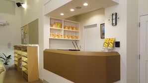 A reception area with a brown counter, shelves with yellow plush toys, a clock, and a framed picture on the wall. - Family Lodge Hatagoya Fukuroi (Fukuroi)