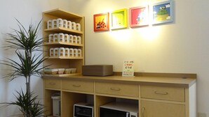 A kitchenette with a microwave, toaster, and shelves with jars. There are framed pictures on the wall and a potted plant. - Family Lodge Hatagoya Fukuroi (Fukuroi)
