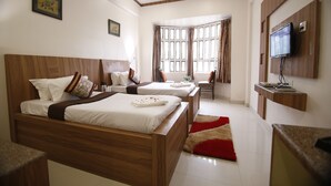 A hotel room with two beds, a TV mounted on the wall, and a large window with curtains. - Hotel Sheetal Regency (Mathura)