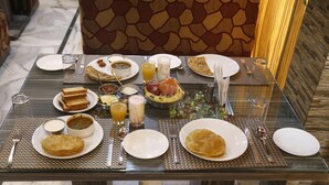 A breakfast table set with various dishes, including flatbreads, a fruit bowl, and a glass of orange juice. - Hotel Sheetal Regency (Mathura)