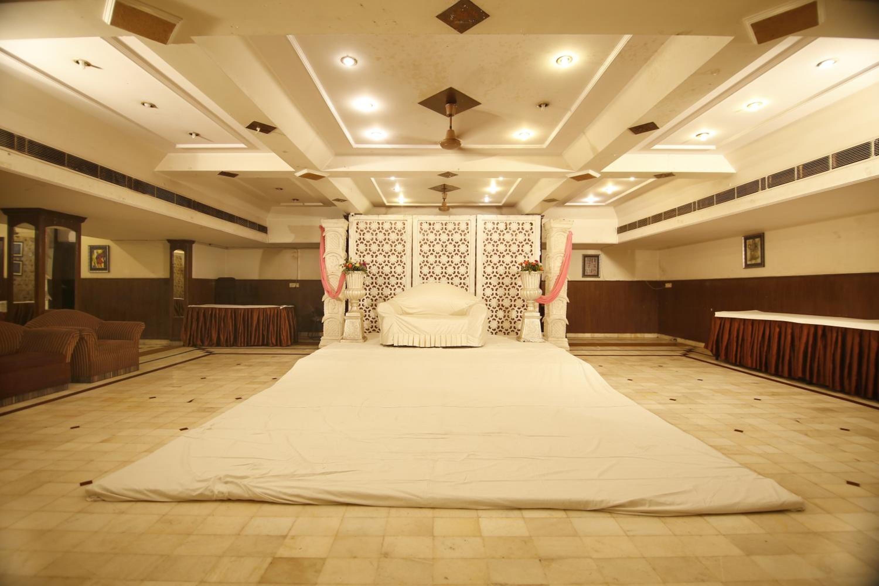 A large, empty room with a central bed, patterned wall decorations, and a ceiling fan.