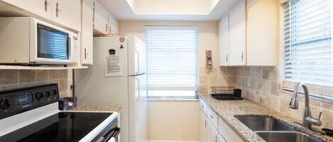 A compact kitchen with a microwave, stove, oven, and granite countertops.
