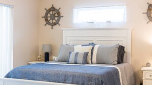 Una camera da letto con un letto, un comodino, una lampada, una finestra e un elemento decorativo al muro.