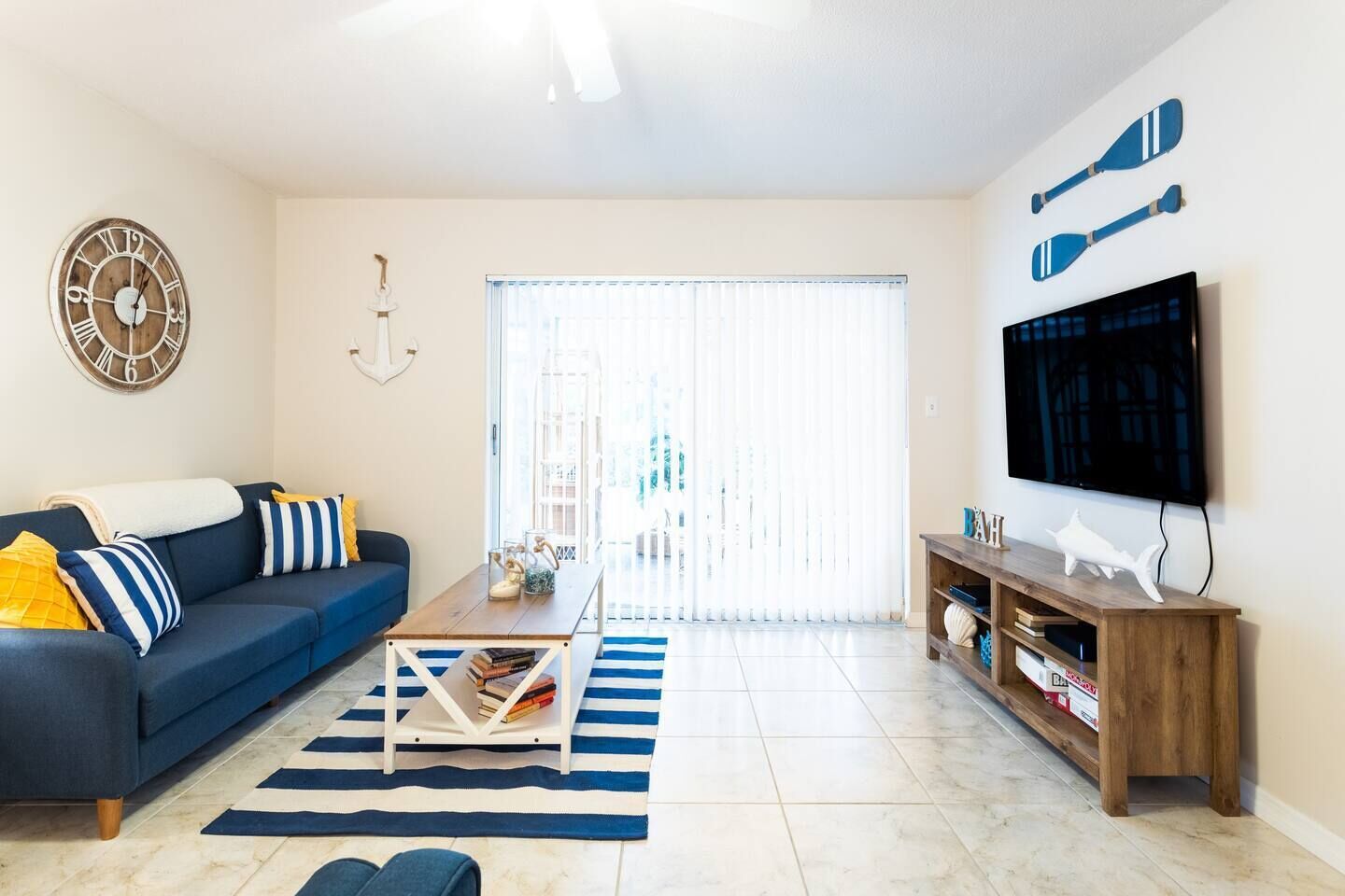 A living room with a sofa, coffee table, TV, and a large window with blinds.