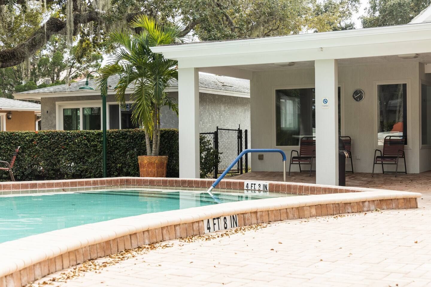 A swimming pool with a 4 FT 8 IN depth marker, surrounded by a covered patio area with chairs and a table.