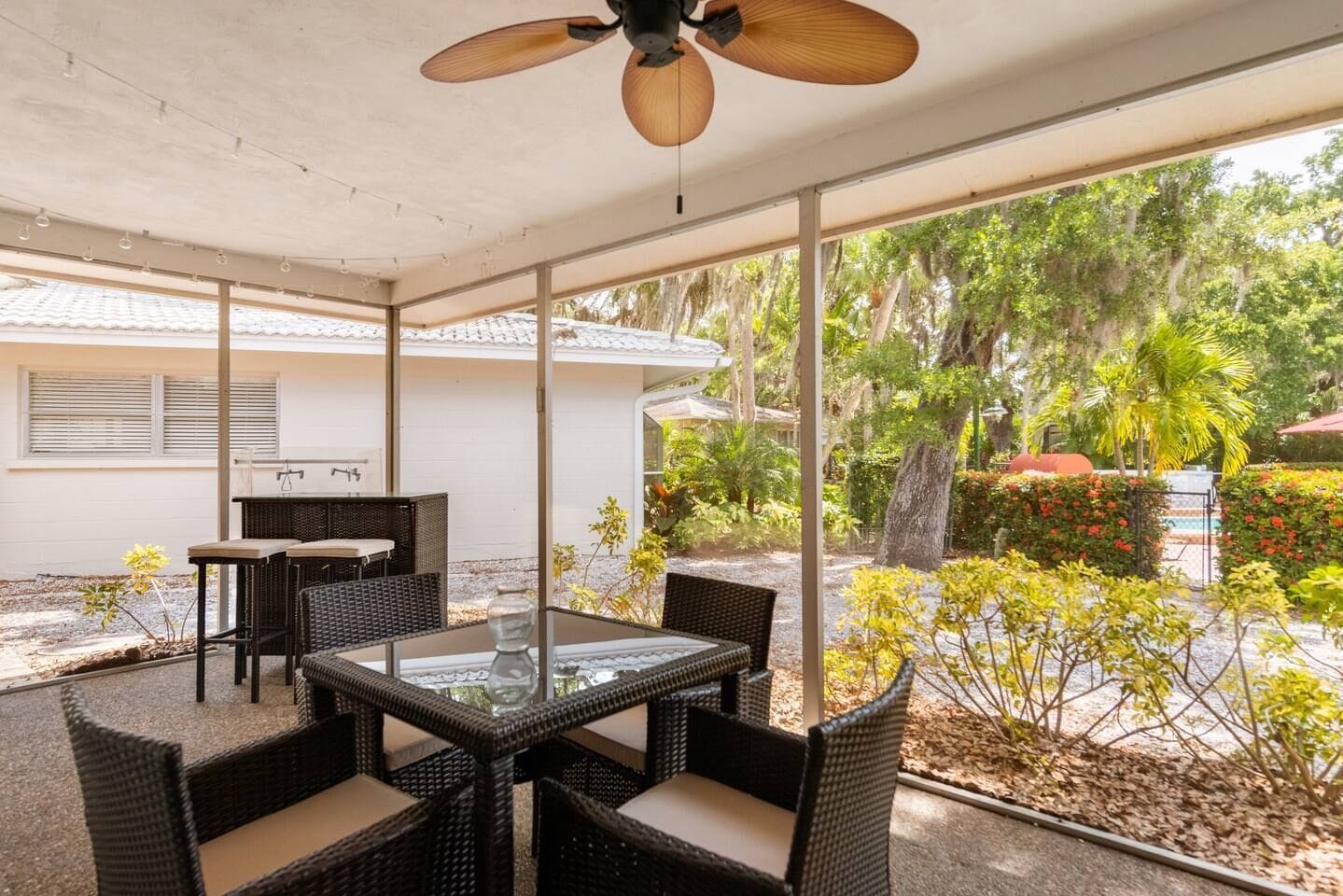 Eine Terrasse im Freien mit Korbmöbeln, einem Glastisch und einem Deckenventilator.