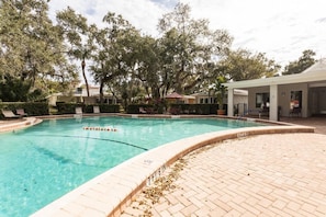 Une piscine dotée d’une terrasse carrelée, entourée d’arbres et agrémentée d’un espace salon abrité.