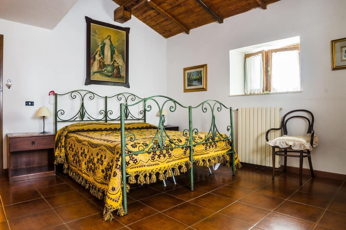 A bedroom with a bed, a chair, a radiator, a window, and a painting on the wall.