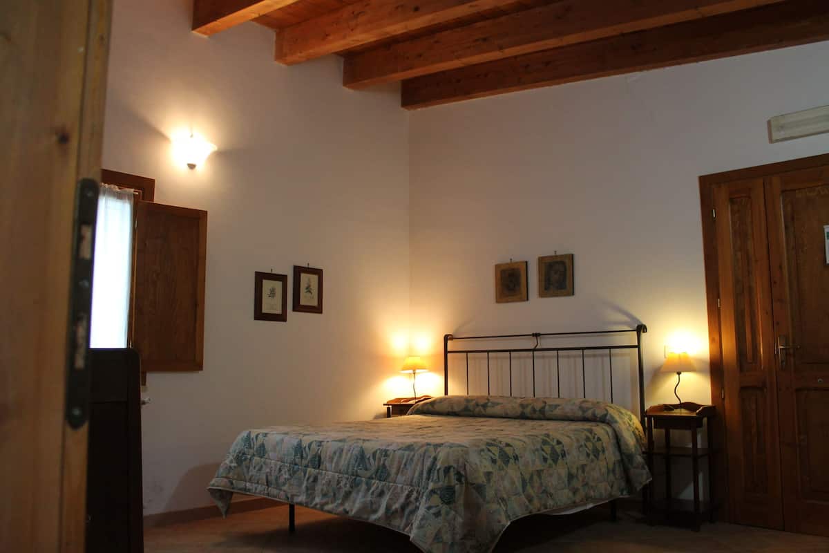 A bedroom with a bed, bedside lamps, wooden ceiling beams, and a door.