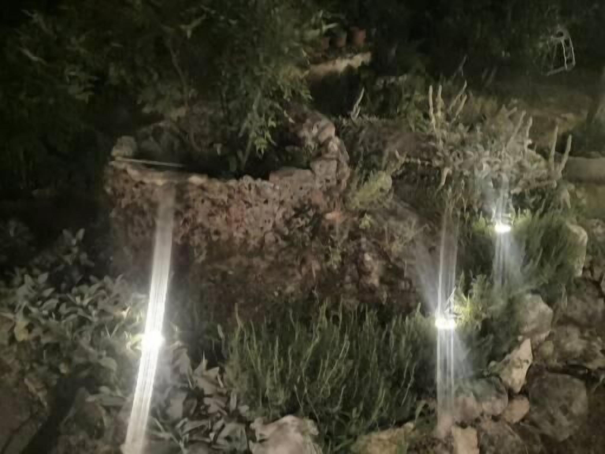 A nighttime view of a garden with two illuminated water features and a rocky terrain.