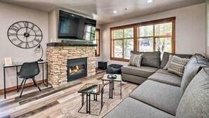 A living room with a stone fireplace, a large clock, a sofa, and a television. - Solitude Mountain Resort Condo at Lift Base! (Solitude)