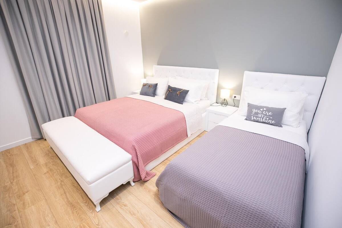 Habitación de hotel con dos camas, un banco y una mesita de noche con lámpara.