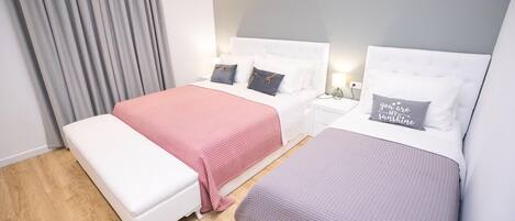 Quarto de hotel com duas camas, um banquinho e uma mesa de cabeceira com abajur.